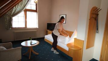 A hotel room with a bed, a small round table with a vase, a TV, and a coat rack.