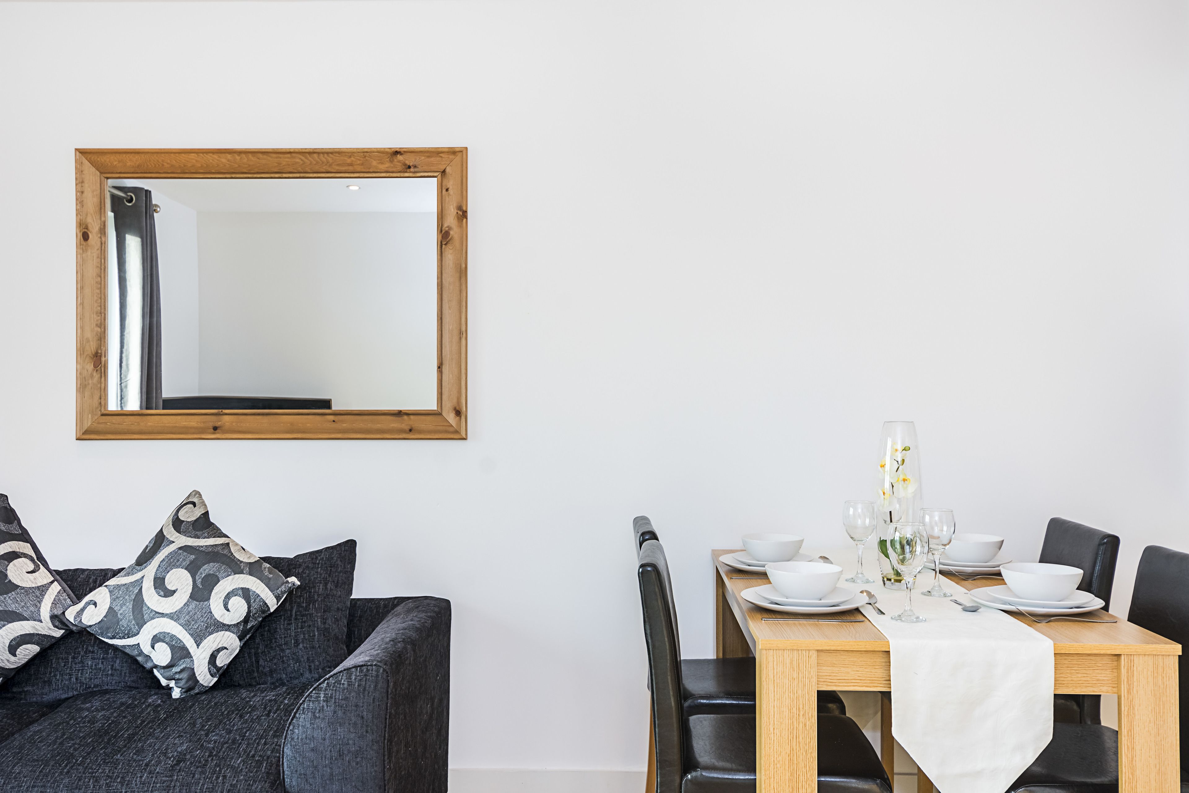 A dining area with a wooden table set for four, accompanied by a sofa with patterned cushions.