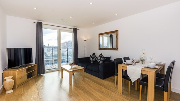 A modern living room with a sofa, dining table, and TV. - Highlife Lexington Apartments (Slough)