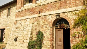 A rustic stone building with a wooden door, arched windows, and a small garden area with potted plants. - Verdidea - Aia Vecchia (Asciano)