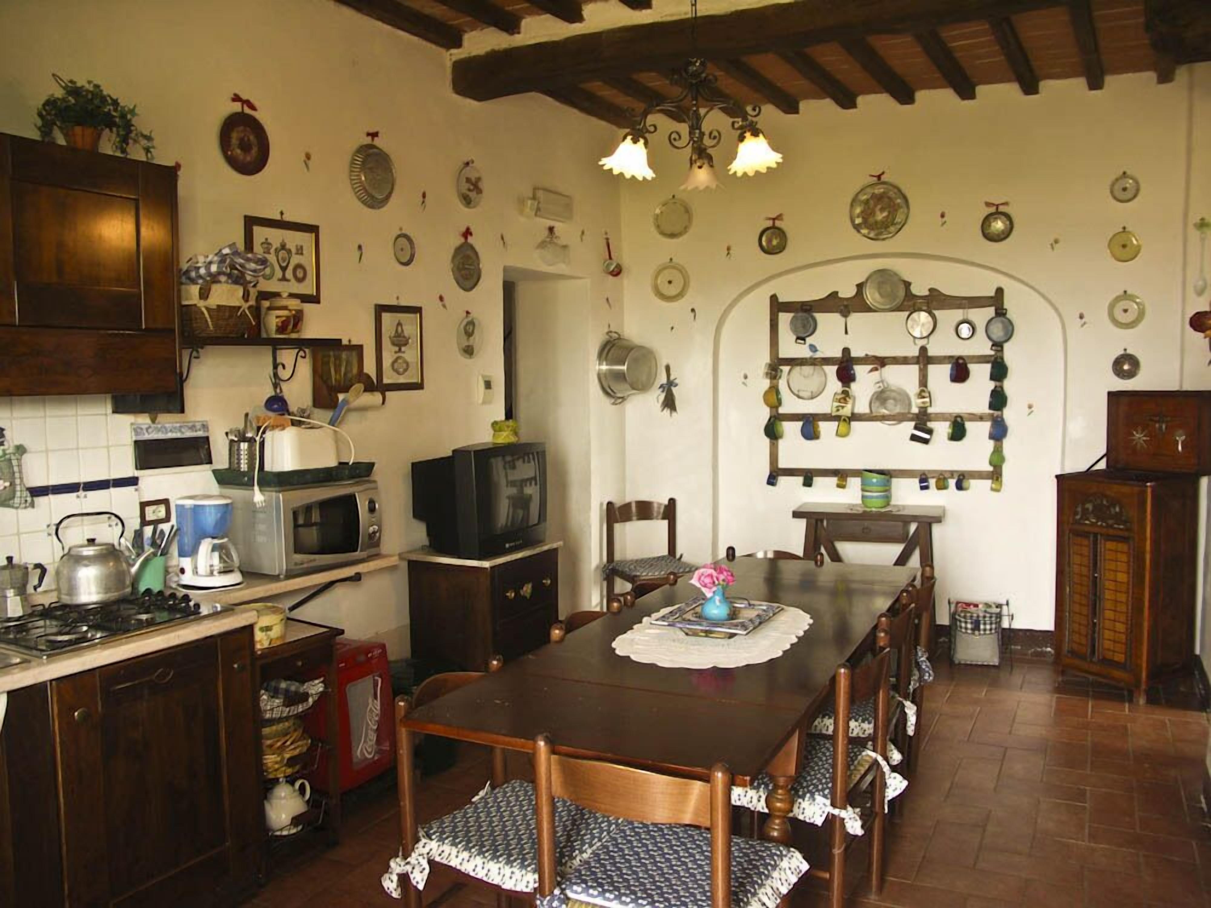 Une cuisine avec des meubles de rangement en bois, une table à manger avec des chaises et un porte-casseroles fixé au mur.