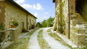 A narrow cobblestone path flanked by rustic stone buildings with arched doorways and potted plants. - Verdidea - Aia Vecchia (Asciano)