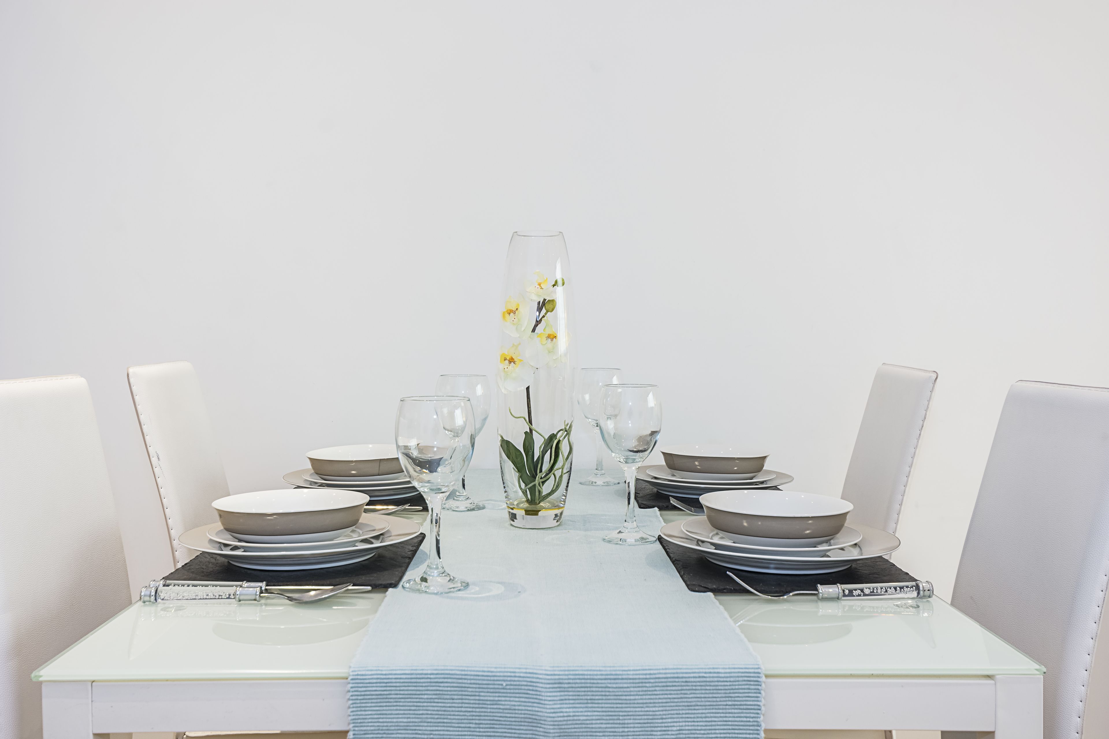 A dining table set with plates, bowls, and glasses, centered with a vase of flowers.