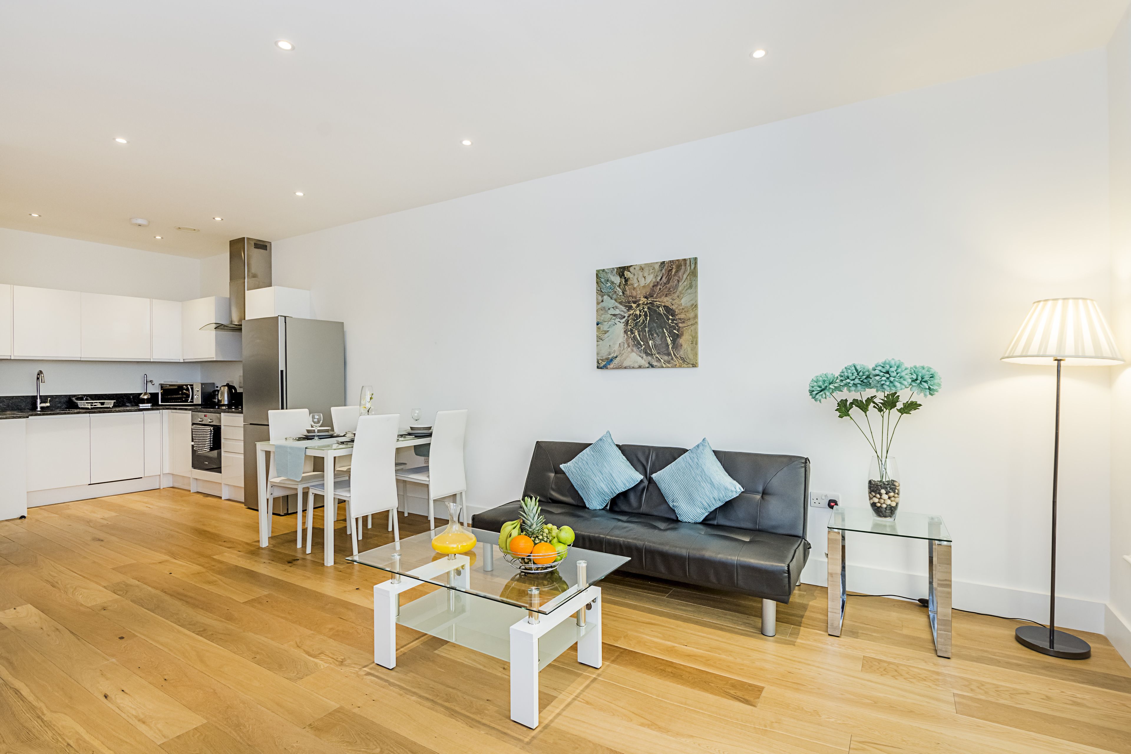 A modern living room with a glass coffee table, a black leather sofa, and a dining area with white chairs.