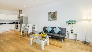 A modern living room with a glass coffee table, a black leather sofa, and a dining area with white chairs.