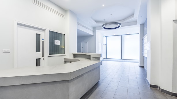 A modern hotel lobby with a reception desk, a large window, and a tiled floor.