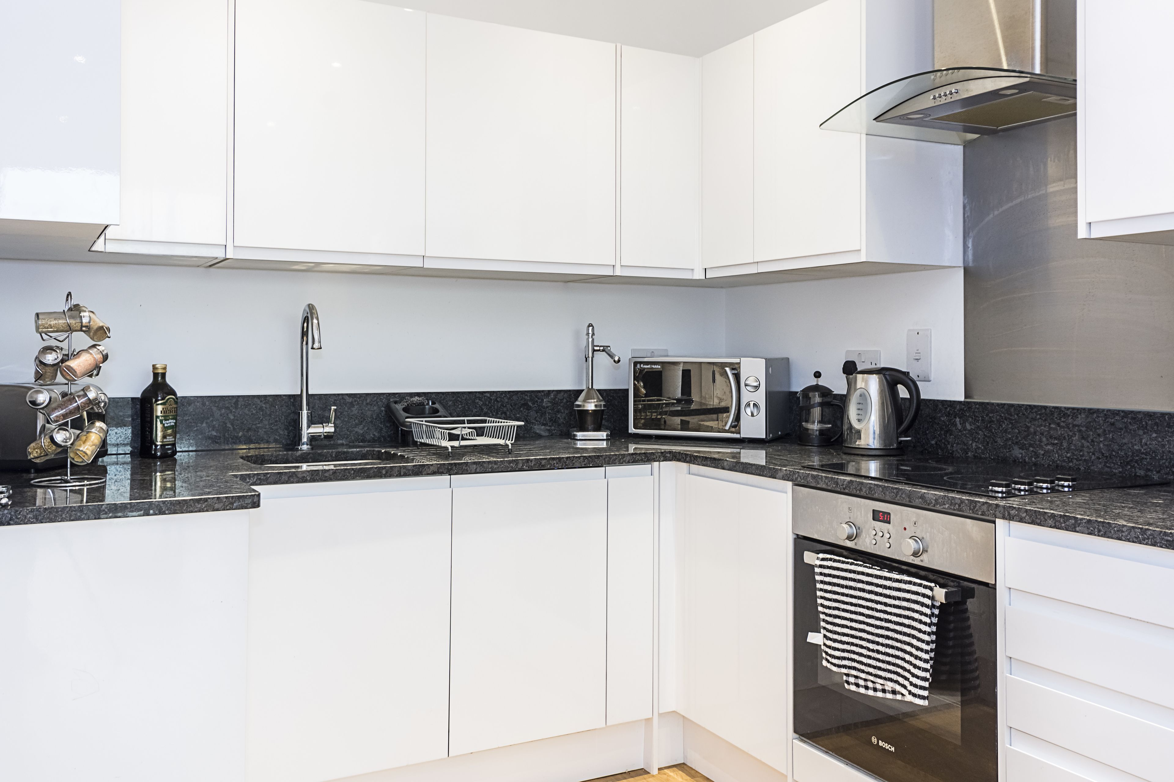 A modern kitchen with white cabinets, a built-in oven, a microwave, and a coffee maker.