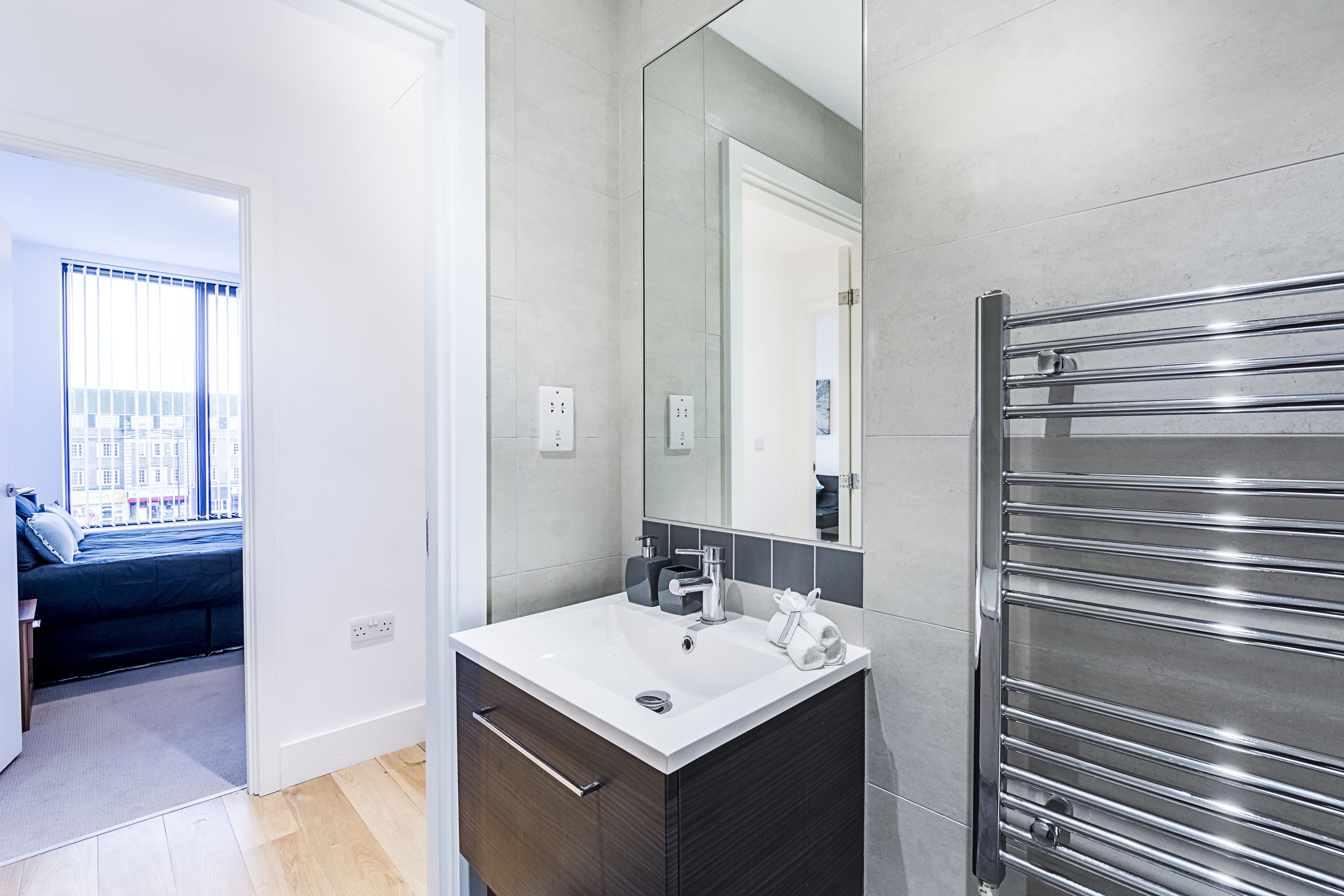 A modern bathroom with a large mirror, a white sink, and a chrome towel rack.
