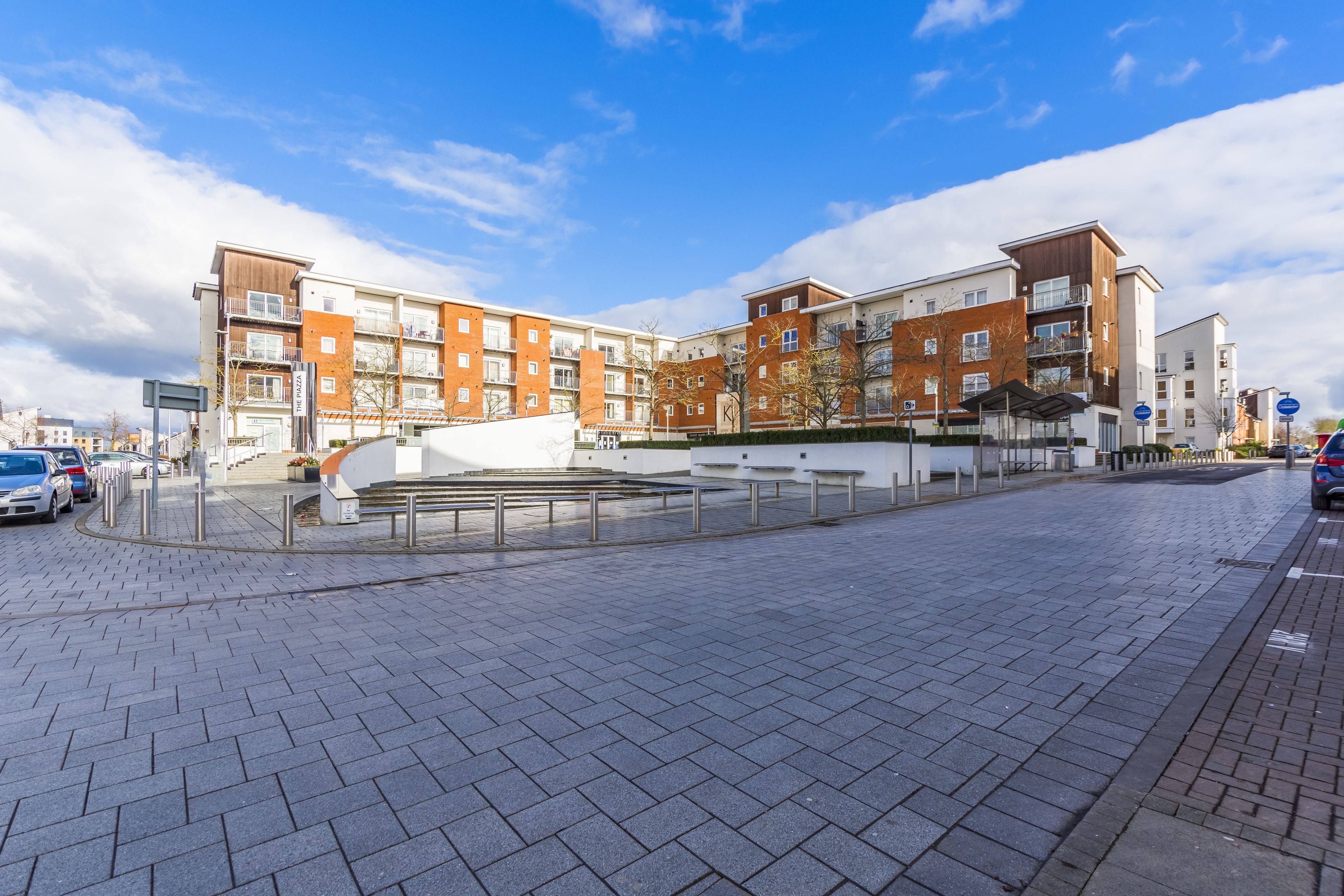 A modern apartment building with a brick facade, multiple balconies, and a paved courtyard.