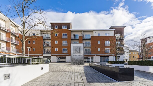 A modern apartment building with a prominent 'KI' sign, a paved courtyard, and a clear blue sky. - Merrick House Apartments (Reading)