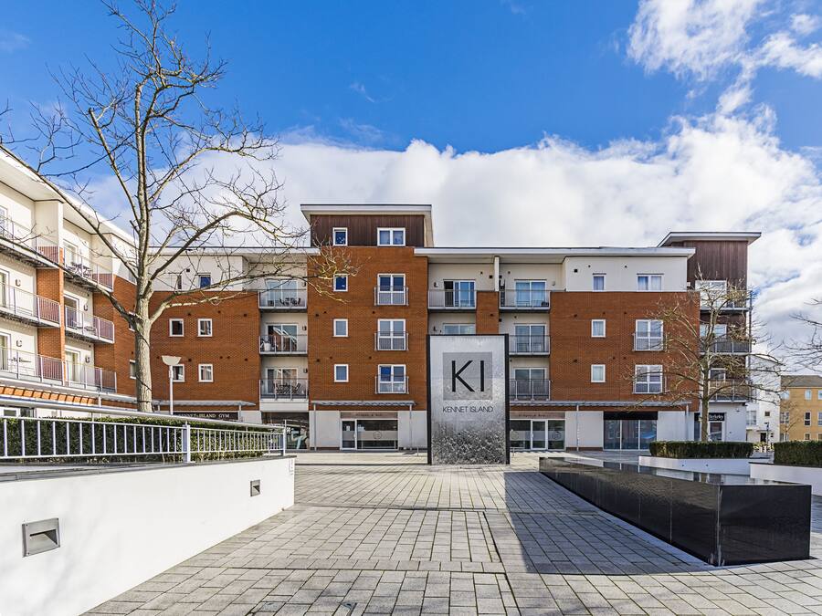 Un moderno edificio residenziale con un evidente cartello 'KI', un cortile lastricato e un cielo azzurro.