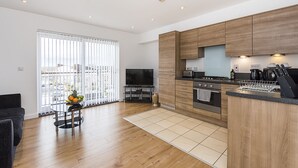 A modern kitchen with wooden cabinets, a built-in oven, and a dining area with a TV. - Merrick House Apartments (Reading)