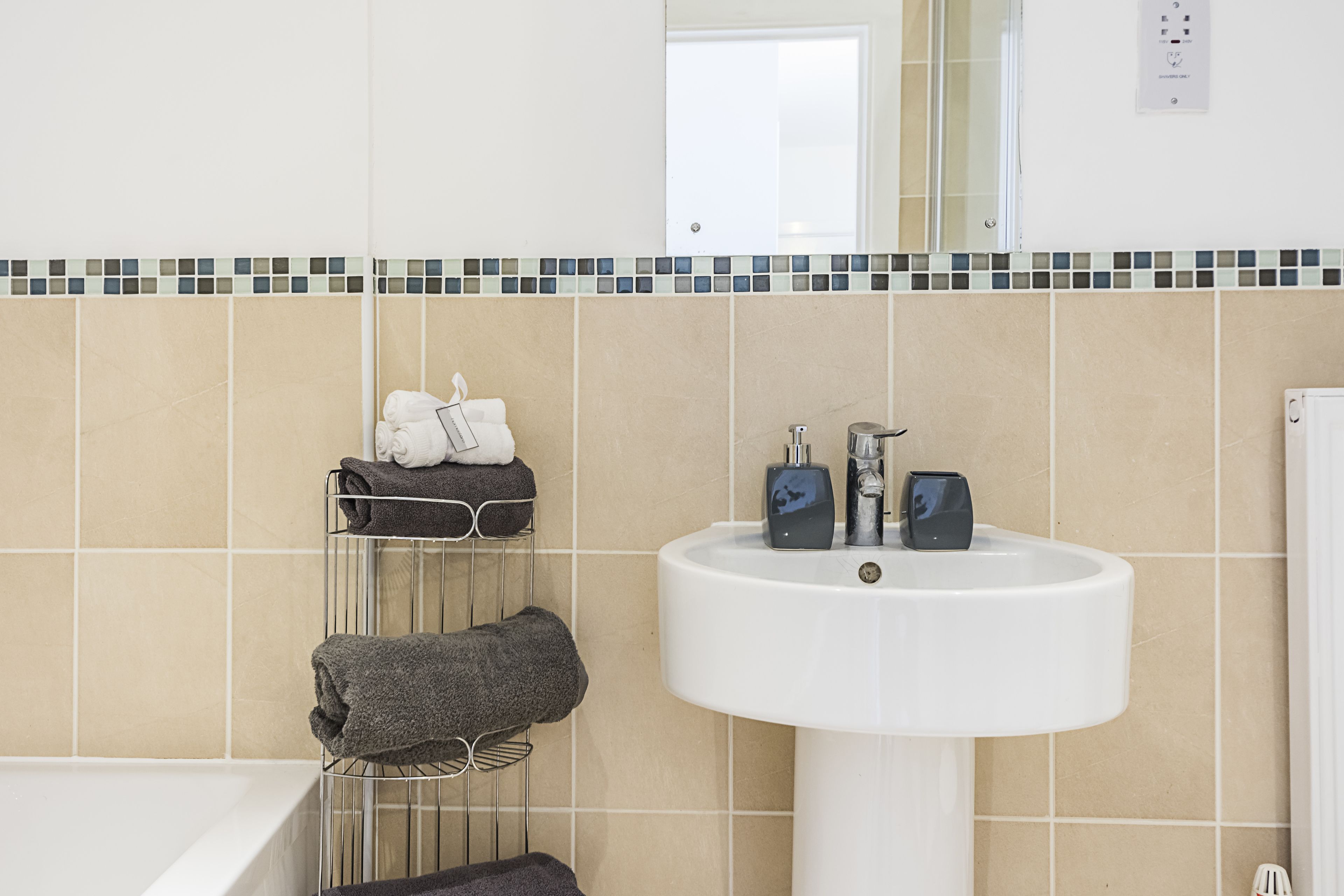 Une salle de bain avec un lavabo blanc, un porte-serviettes avec des serviettes et un mur recouvert de carreaux.