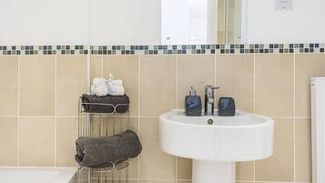 Une salle de bain avec un lavabo blanc, un porte-serviettes avec des serviettes et un mur recouvert de carreaux.