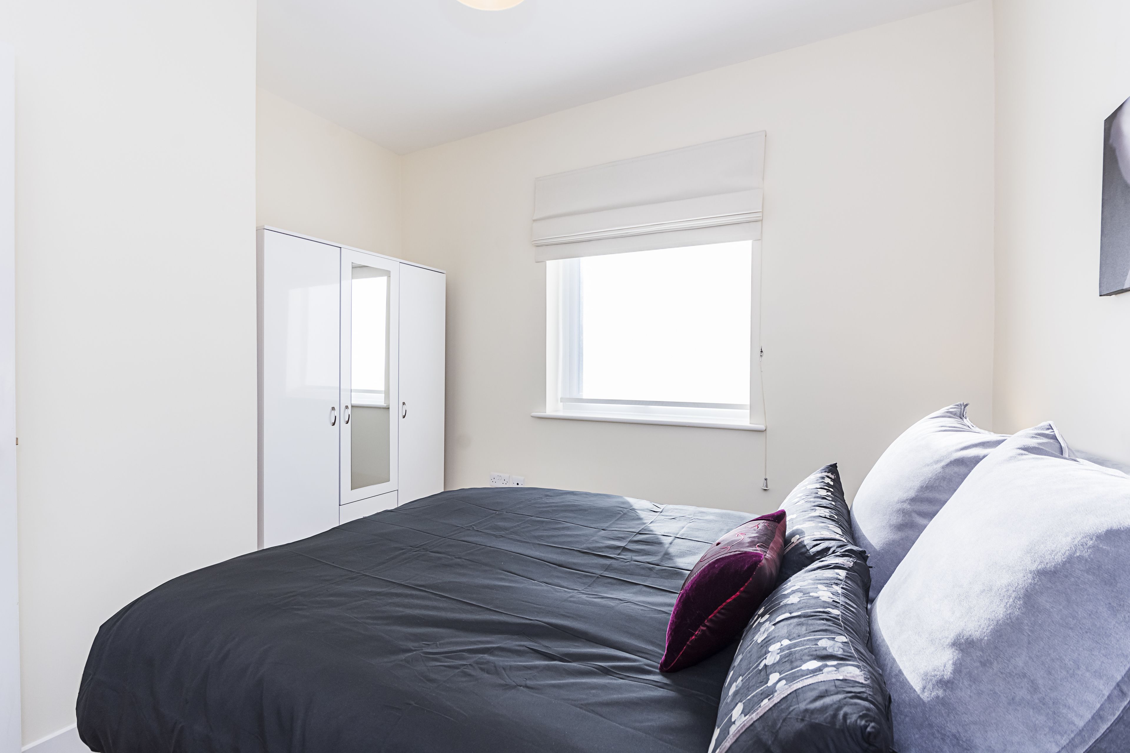 A bedroom with a bed, a wardrobe, a window, and a wall-mounted light fixture.