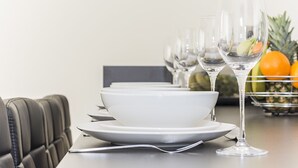 A dining table set with white plates, bowls, and wine glasses, with fruits in the background. - Heron House Apartments (Reading)
