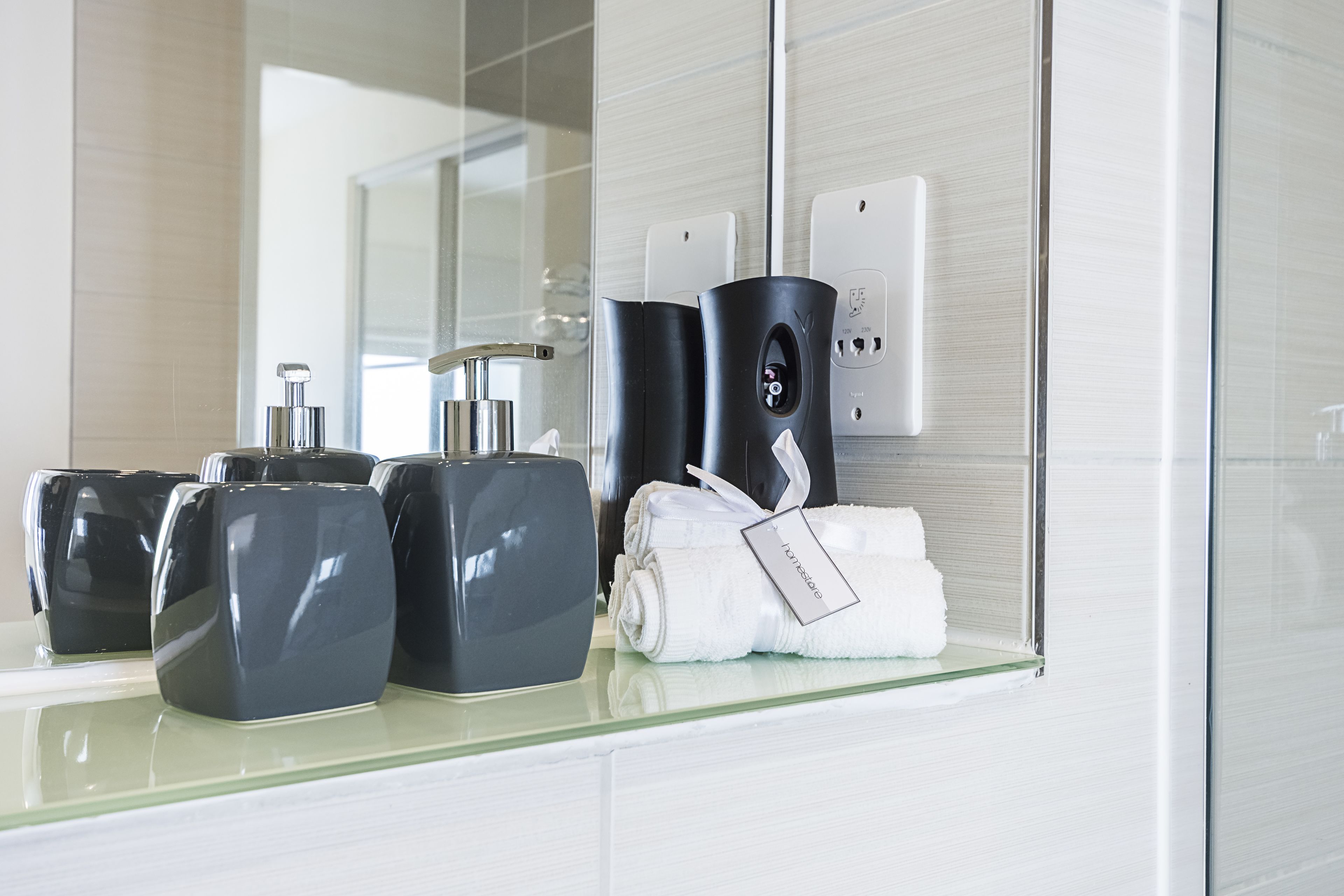 A modern bathroom with a glass countertop, black and white toiletries, and a towel rack.