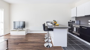 A modern kitchen with a central island, bar stools, a flat-screen TV, and built-in appliances. - Heron House Apartments (Reading)