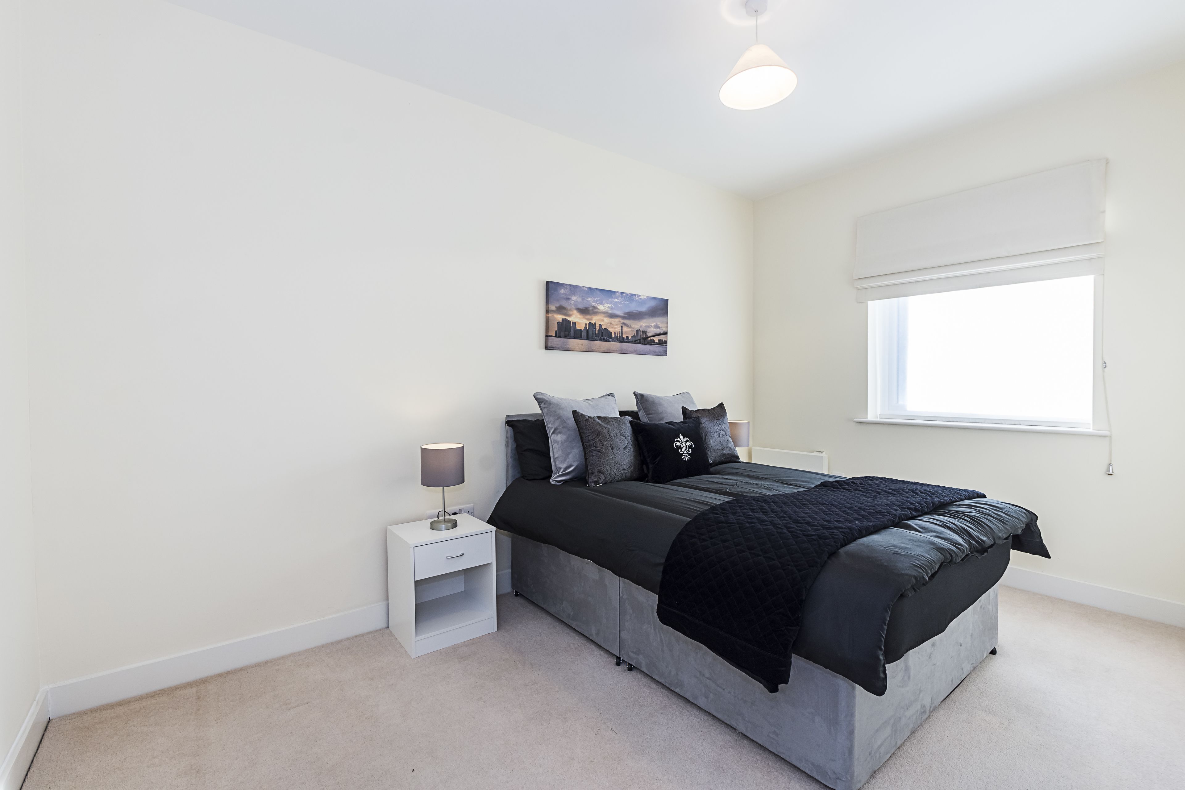 A bedroom with a bed, nightstand, and a window.