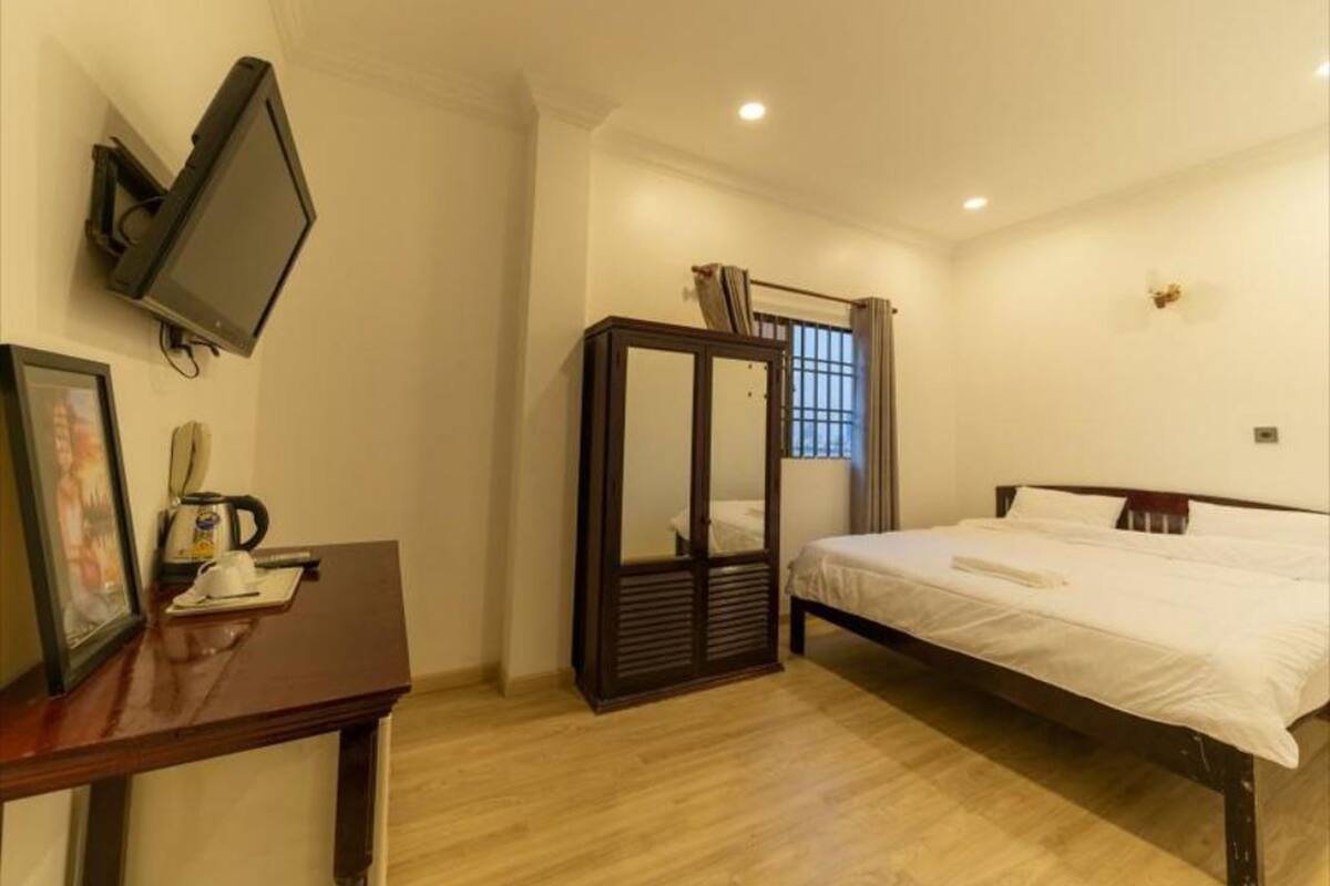 A bedroom with a bed, a desk with a telephone and a coffee maker, a TV mounted on the wall, and a wardrobe with a mirror.