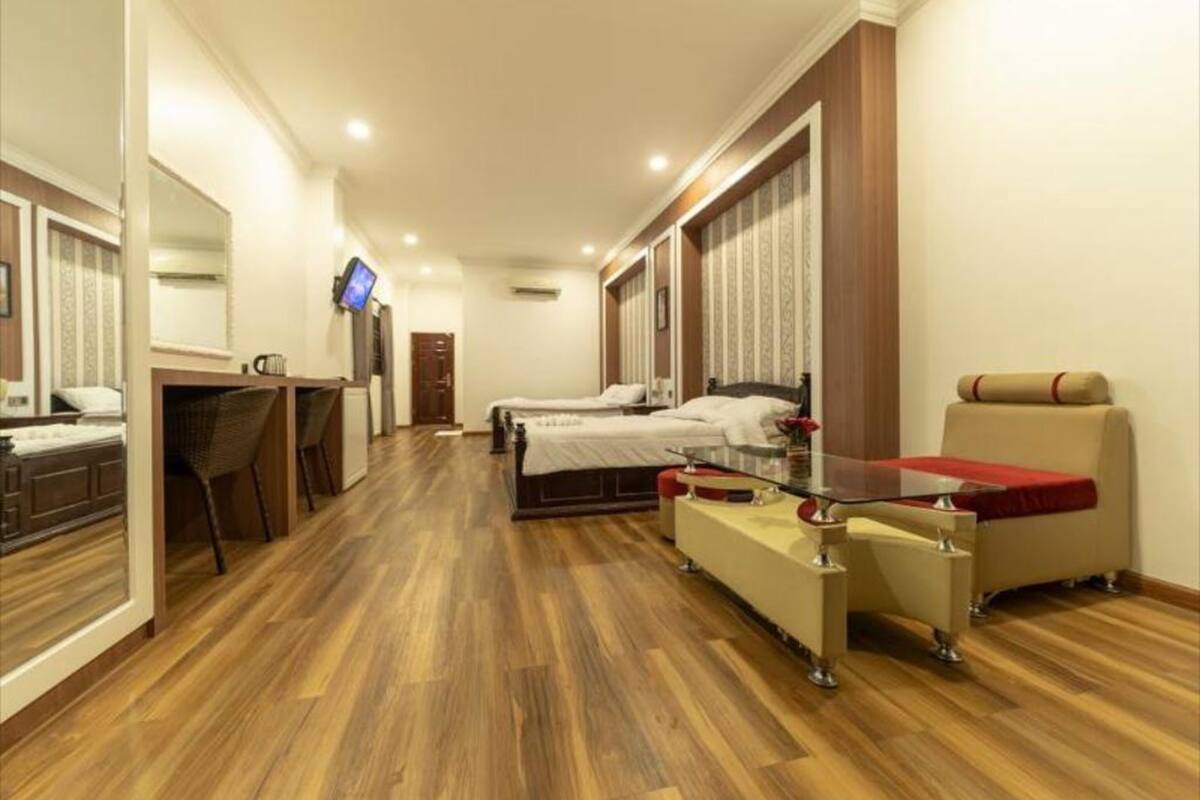 A hotel room with a wooden floor, a bed, a desk with a chair, a TV, and a bathroom with a bathtub and a toilet.