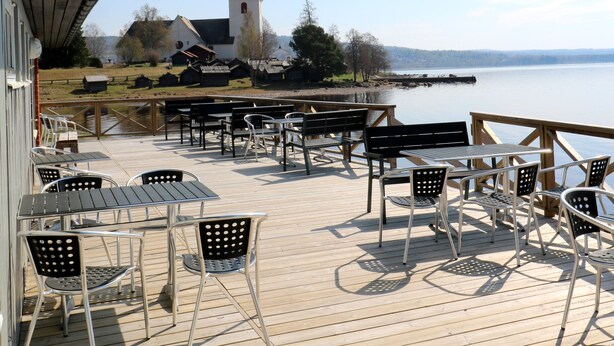 A wooden deck with outdoor seating and a view of a church and water.