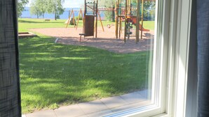A window with a view of a playground and a body of water.