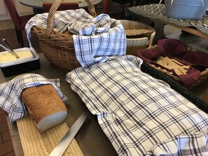 A kitchen counter with a loaf of bread, a knife, a bowl of butter, a wicker basket, and a baking tray.