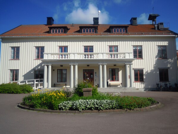 A large white building with a red-tiled roof, multiple windows, and a central entrance with columns.