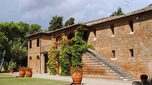 A traditional brick building with a staircase leading to an upper level, surrounded by a well-maintained garden with large terracotta pots. - Verdidea - Il Tinaio (Monteroni d'Arbia)