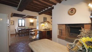 Una cocina rústica con chimenea de ladrillo, vigas de madera y un comedor con mesa y sillas.