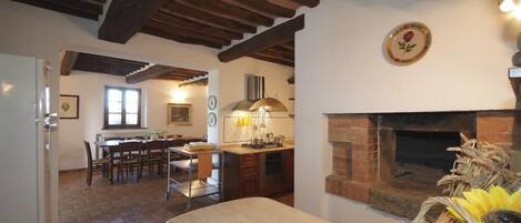 Una cocina rústica con chimenea de ladrillo, vigas de madera y un comedor con mesa y sillas.