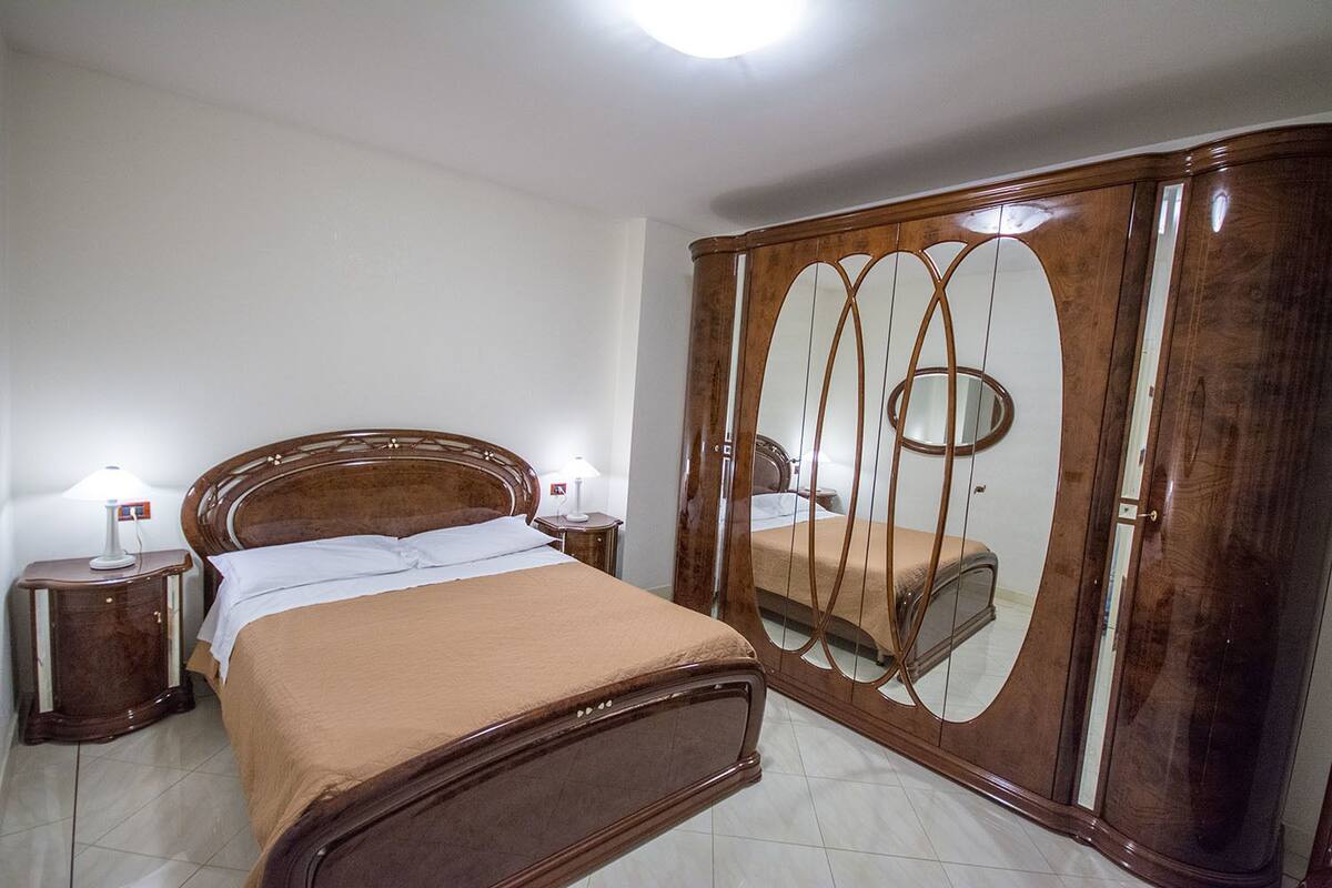 A bedroom with a wooden bed, two bedside tables with lamps, and a large wardrobe with a mirror.