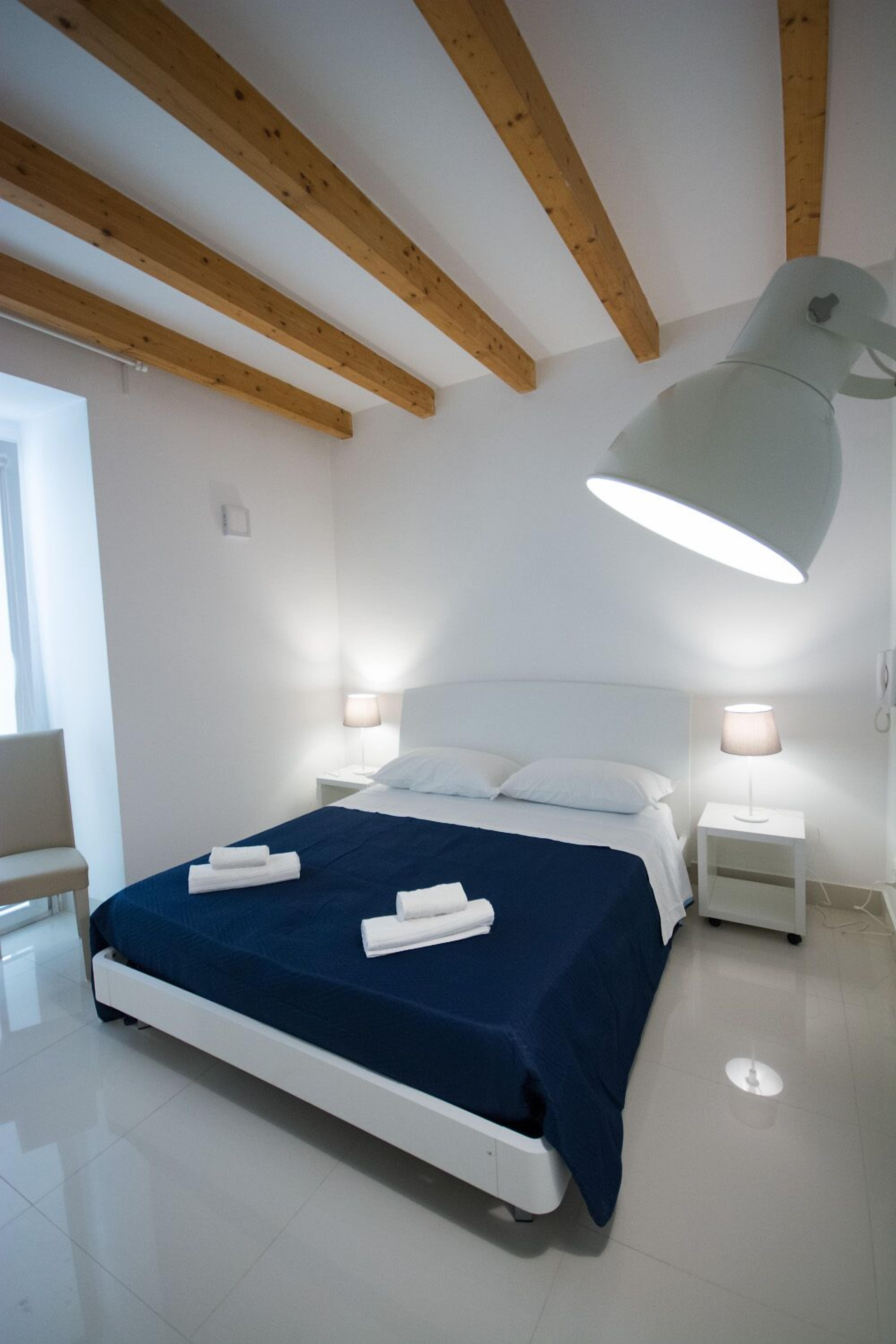 Une chambre moderne avec un grand lit, des poutres en bois au plafond, deux lampes de chevet et une fenêtre avec des rideaux.