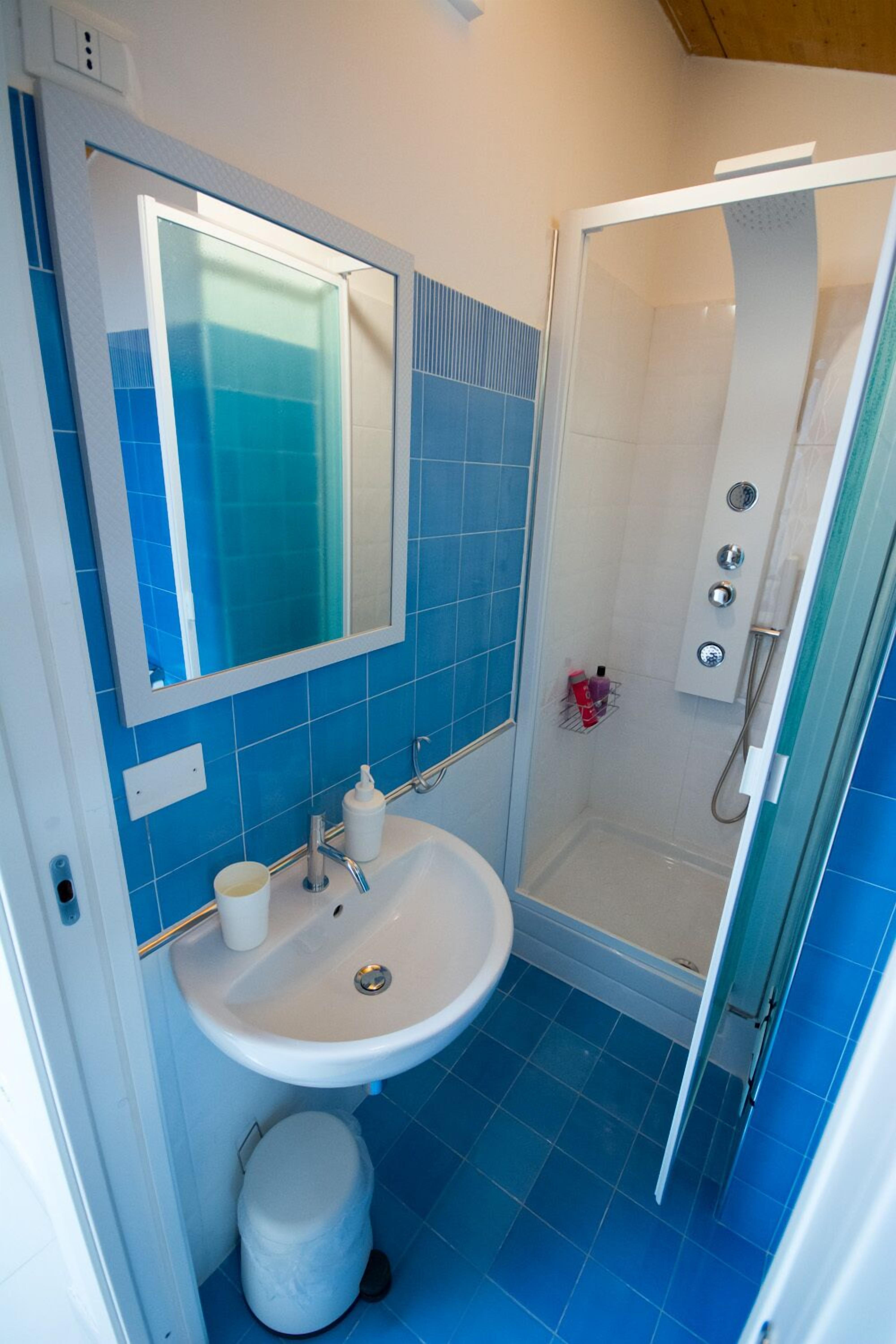 Ein Badezimmer mit Waschbecken in Weiß, blauen Fliesen, einem Spiegel und einer Duschkabine.