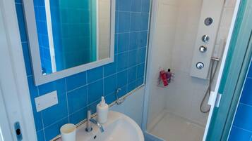 Ein Badezimmer mit Waschbecken in Weiß, blauen Fliesen, einem Spiegel und einer Duschkabine.