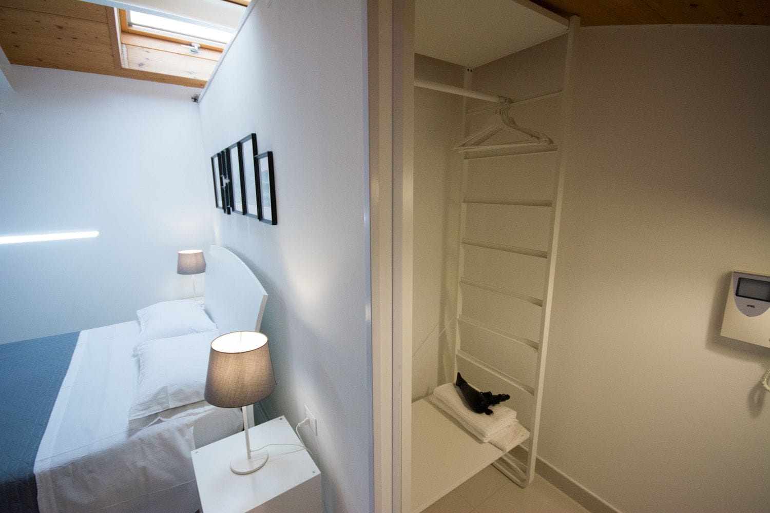 A hotel room with a bed, bedside lamp, and a walk-in closet with a hanging rack and a thermostat.
