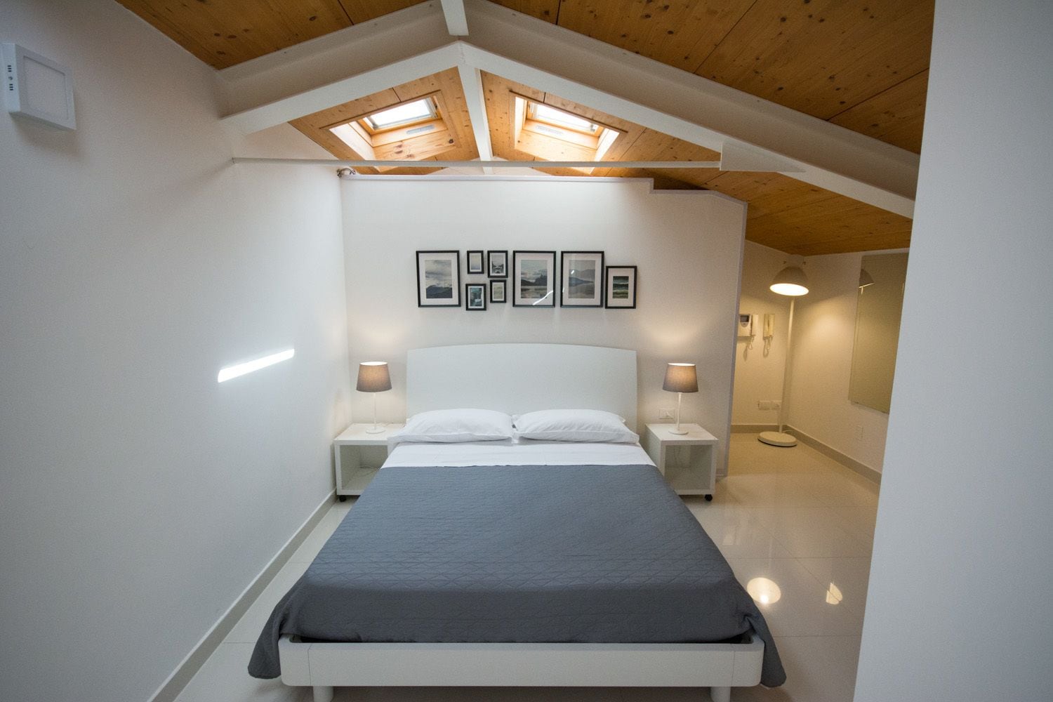 A bedroom with a bed, two bedside tables, a skylight, and framed pictures on the wall.