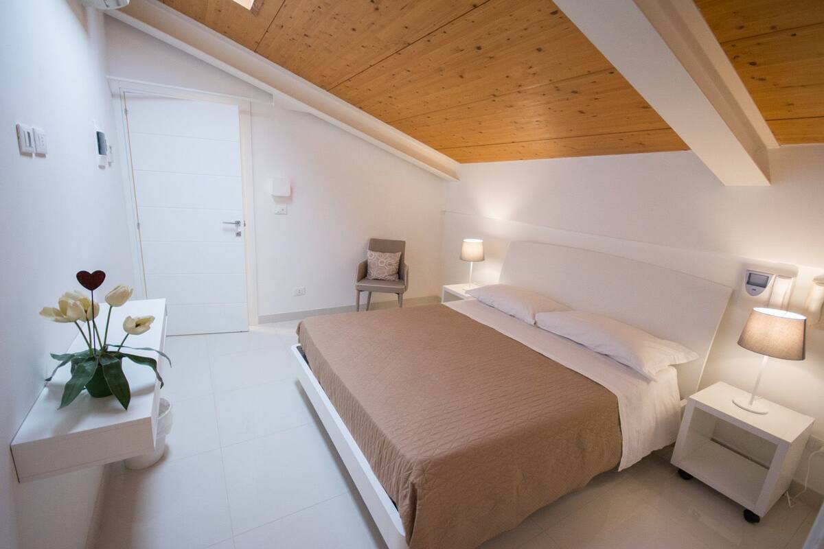 A bedroom with a bed, bedside tables, a chair, and a wall-mounted lamp.