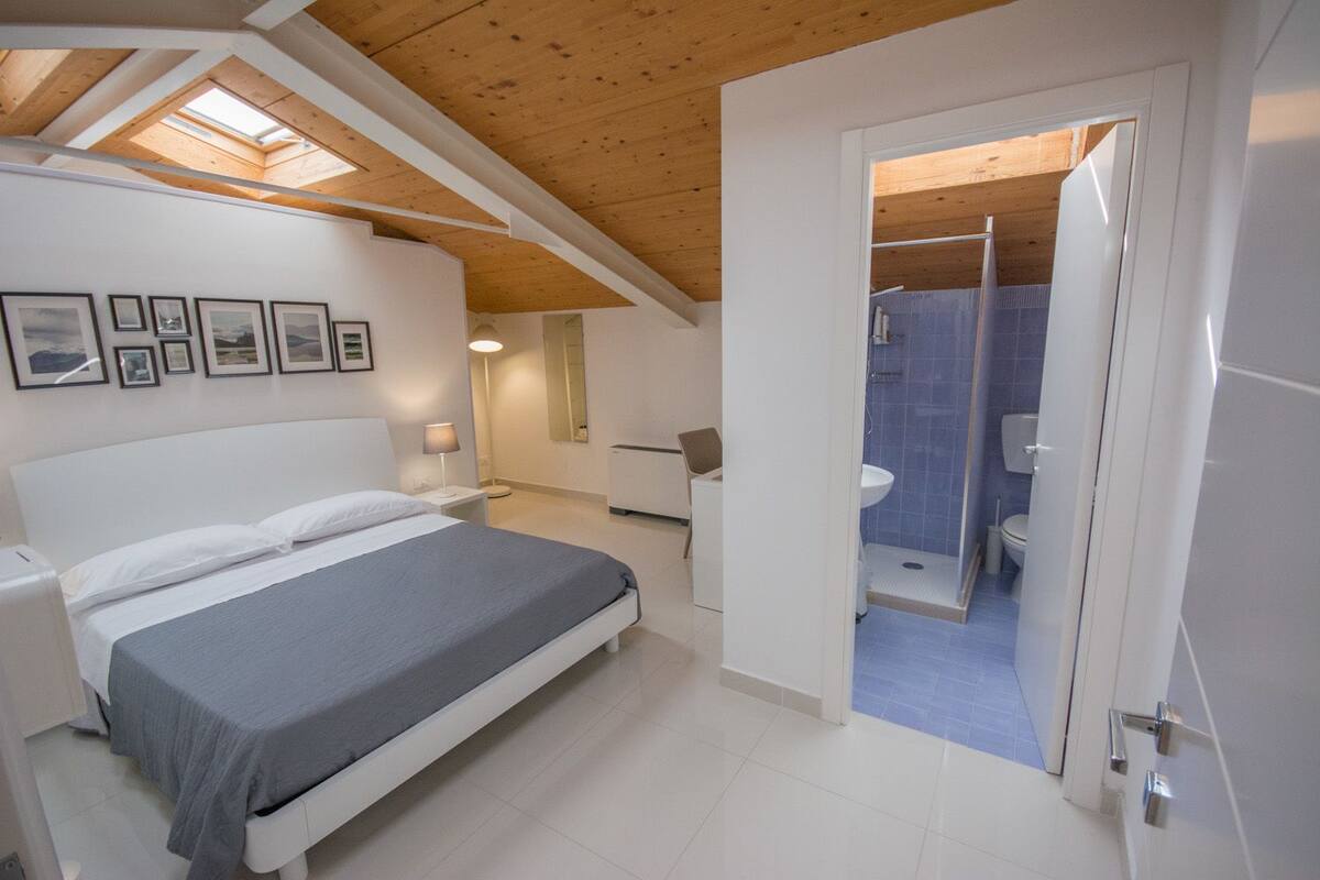 A bedroom with a bed, bedside table, lamp, and framed pictures on the wall.
