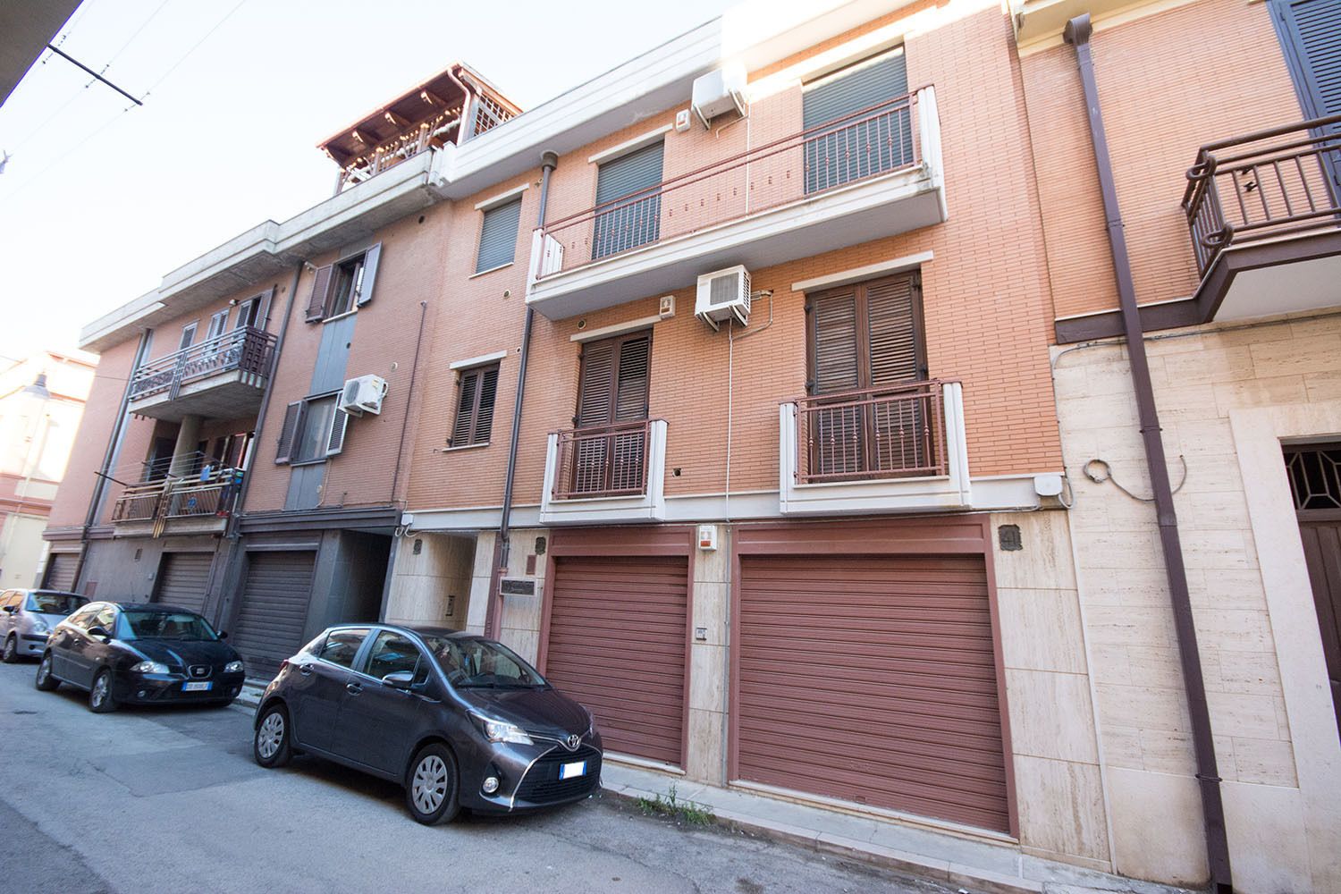 A multi-story residential building with balconies, air conditioning units, and garage doors.