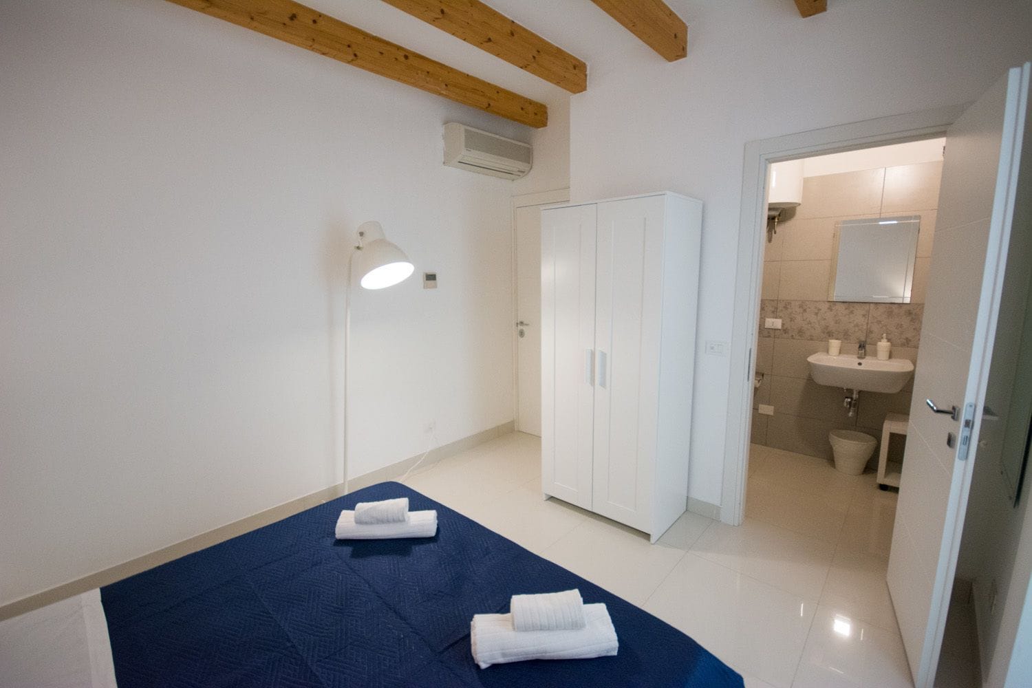 A bedroom with a bed, a wardrobe, and a bathroom visible through an open door.