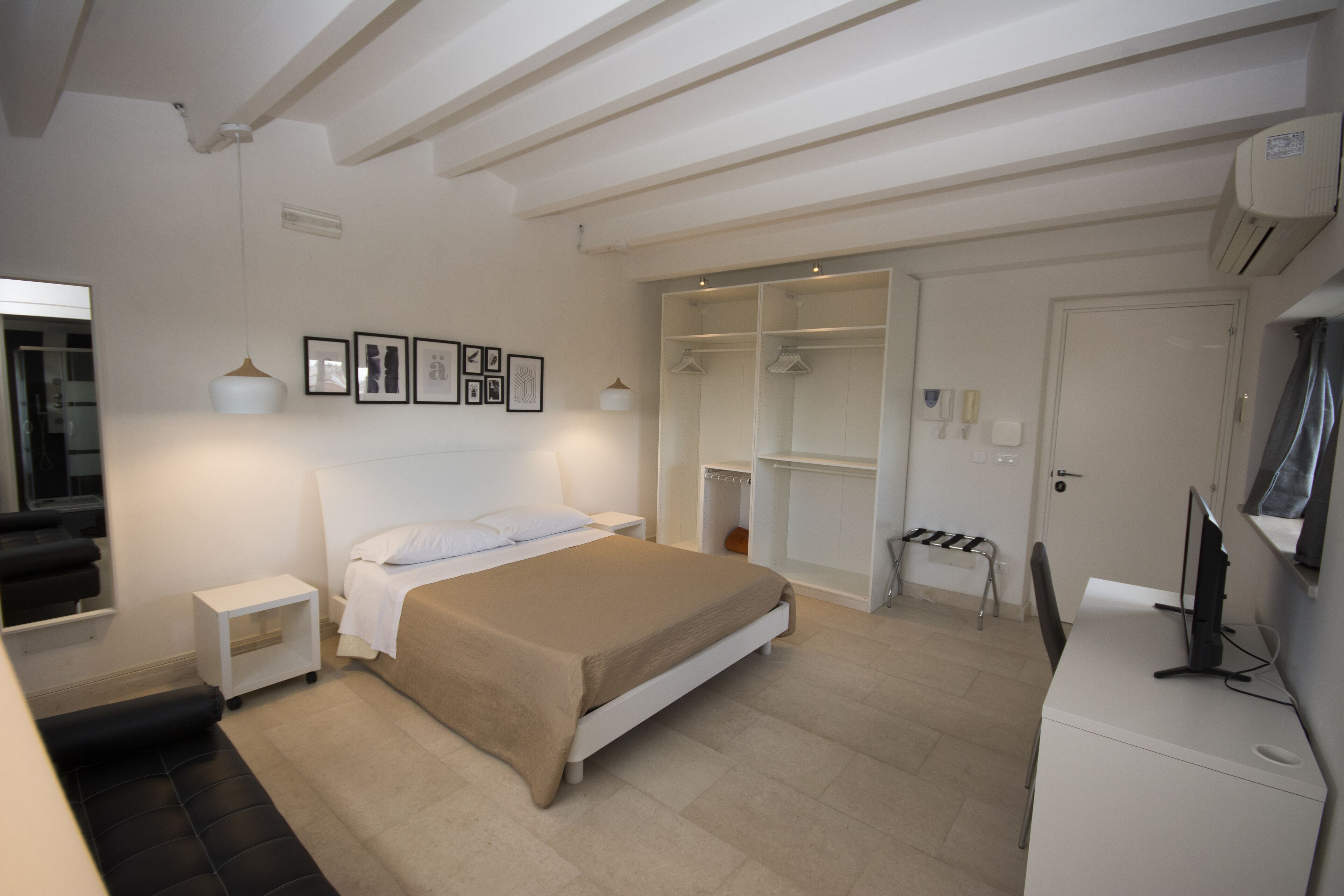 A bedroom with a bed, bedside tables, a desk with a computer, a wardrobe, and a mirror.