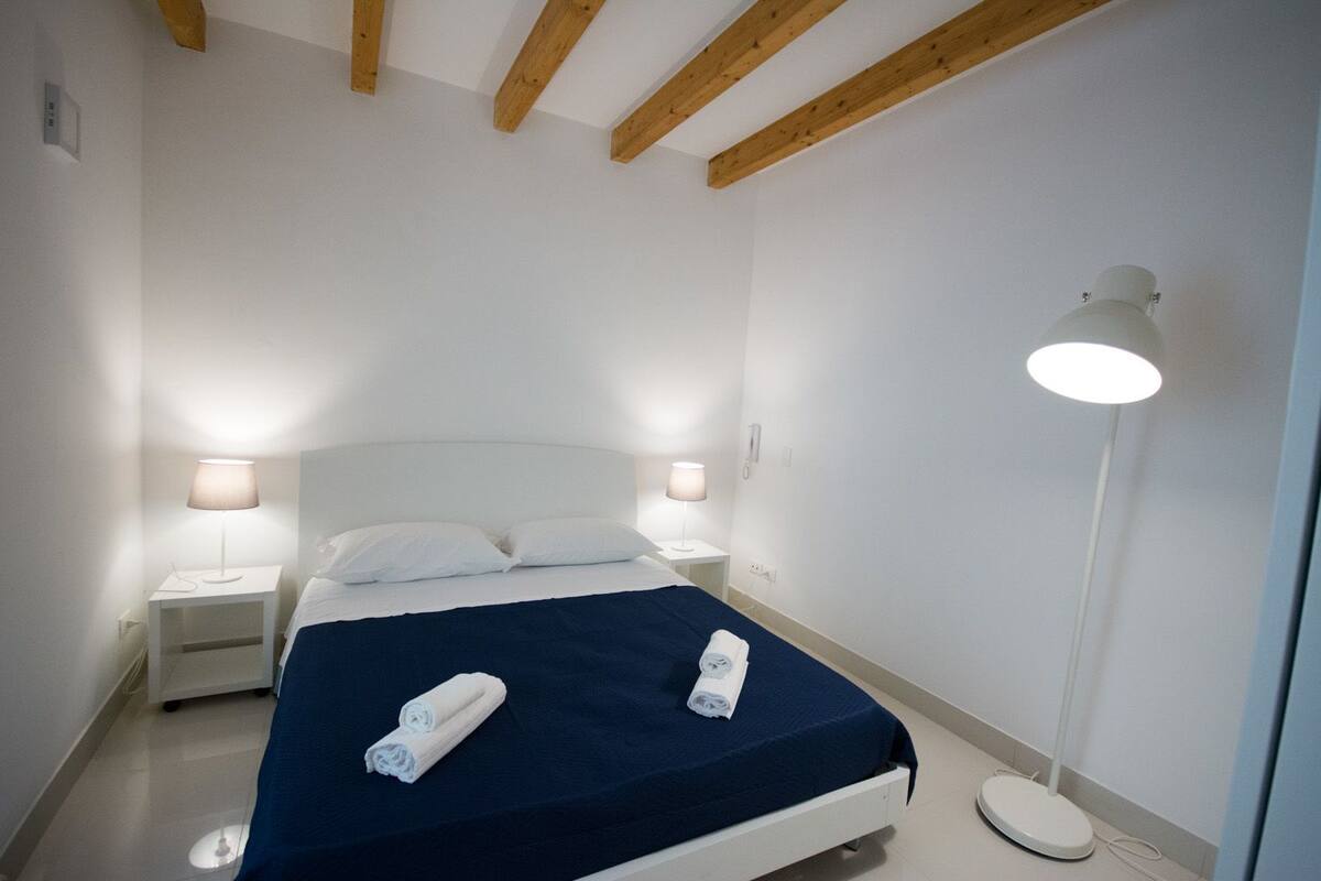 A bedroom with a bed, two bedside lamps, a bedside phone, and a floor lamp.