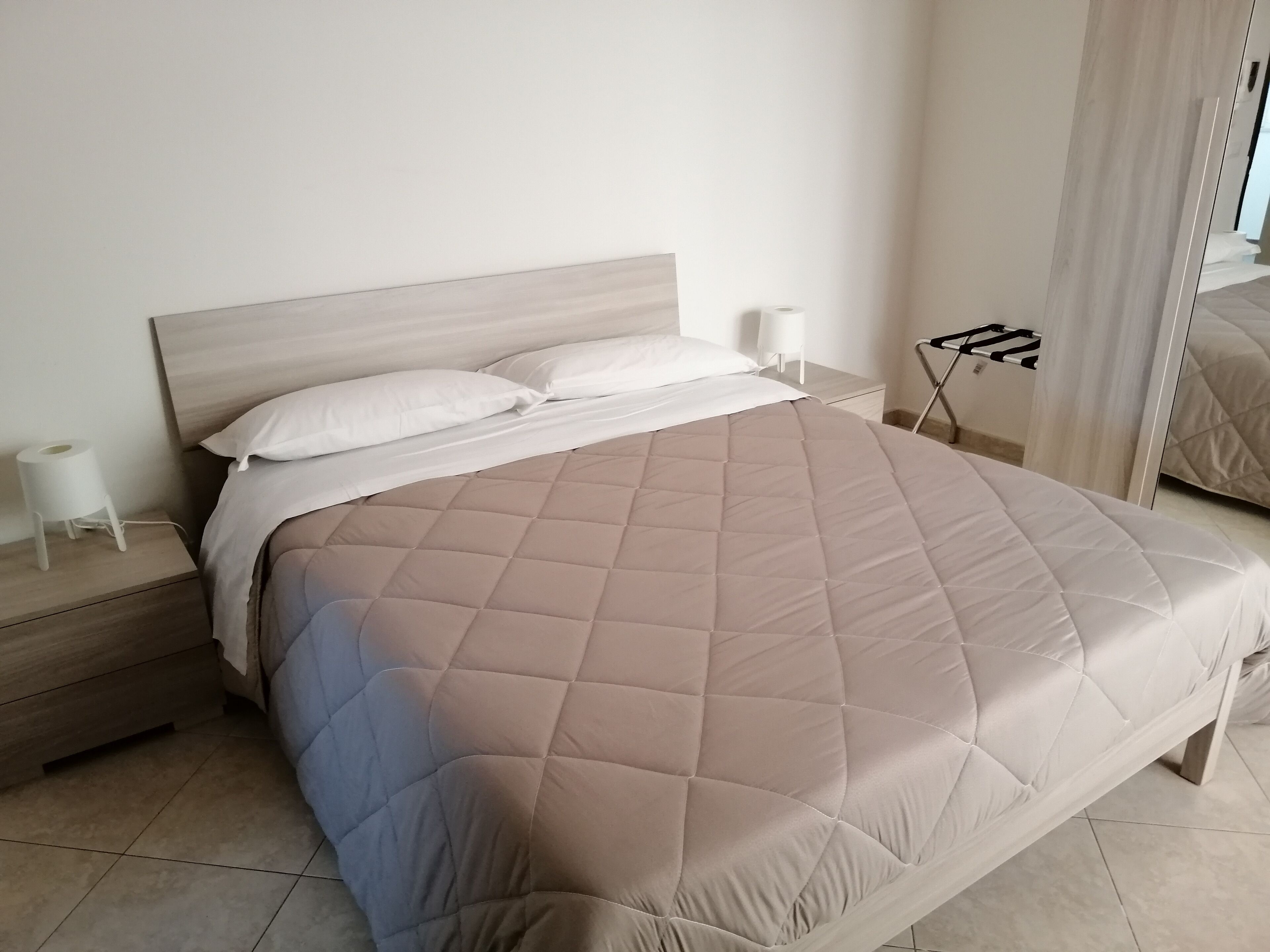 A neatly made bed with a quilted cover, a bedside table with a lamp, and a mirror on the wall.