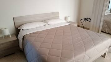 A neatly made bed with a quilted cover, a bedside table with a lamp, and a mirror on the wall.