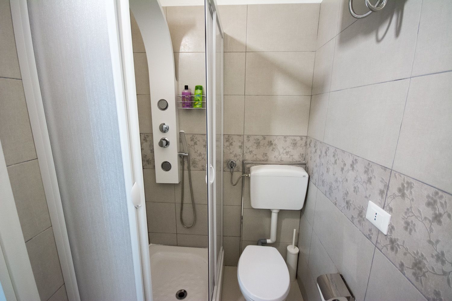 A bathroom with a shower, toilet, and a small shelf with toiletries.
