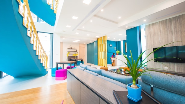 Una sala de estar moderna con una escalera azul, un sofá, un comedor y un televisor.