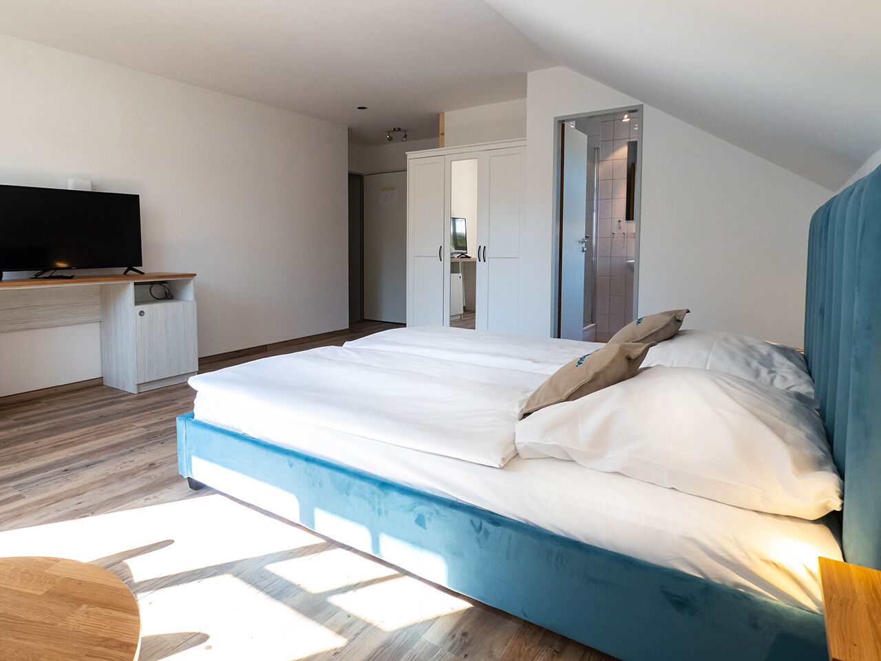 A modern bedroom with a large bed, a TV on a stand, and a wardrobe.