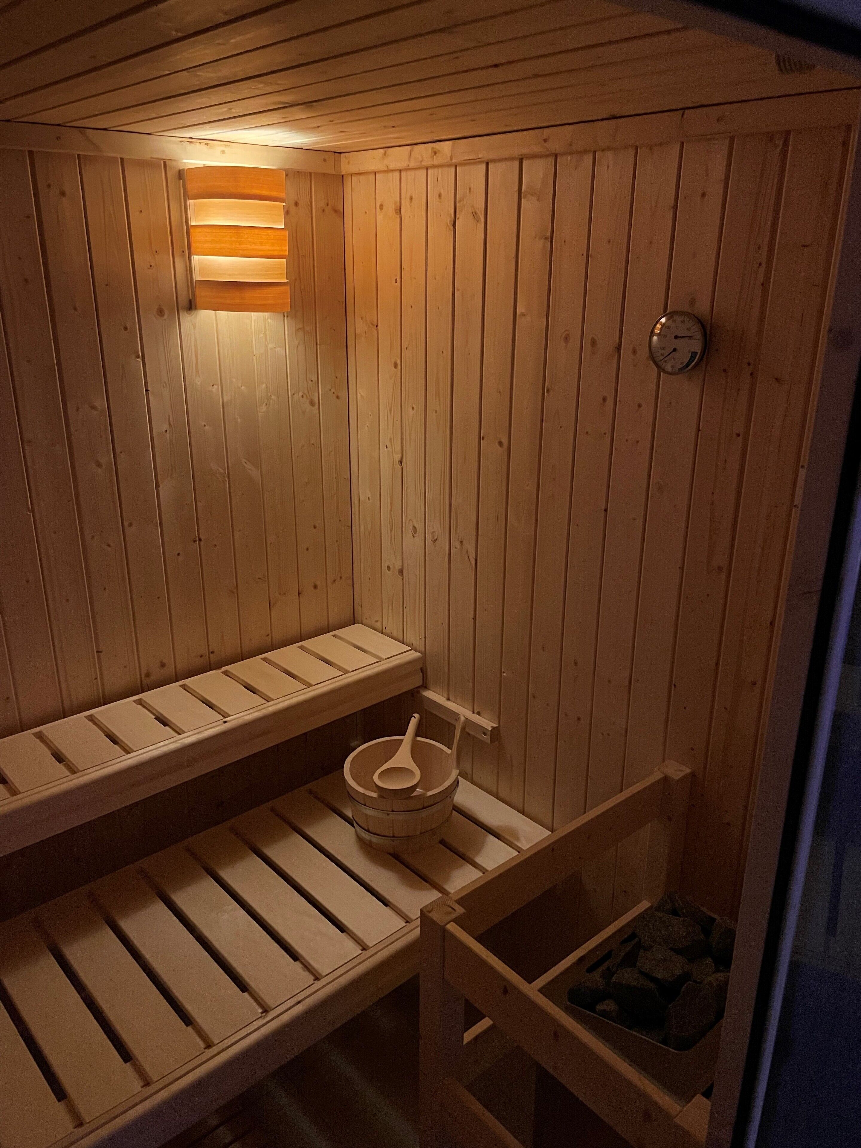A wooden sauna with benches, a bucket, and a clock on the wall.